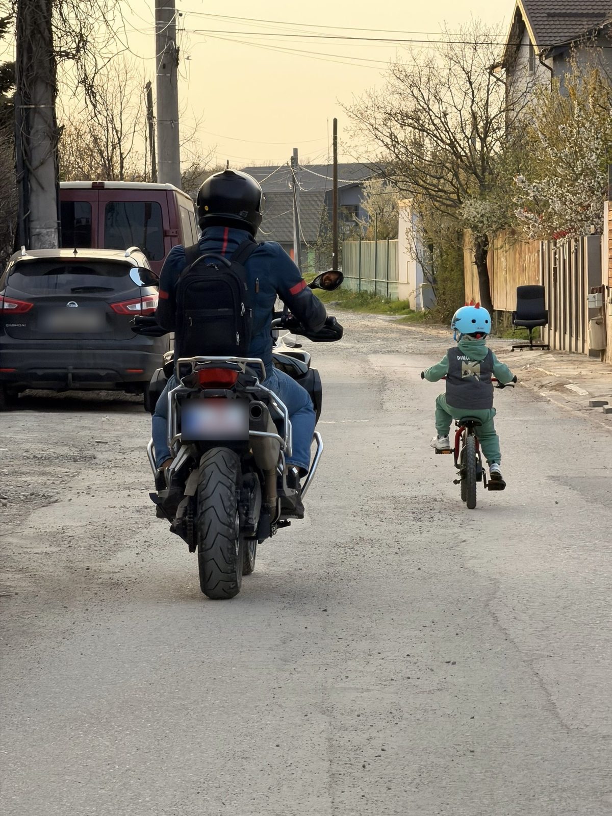 Vlad on his motorcycle and his son on a bicycle, riding down the same street, seen from behind